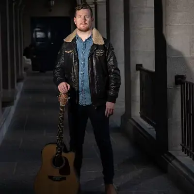 George Murphy in a leather jacket holding his guitar
