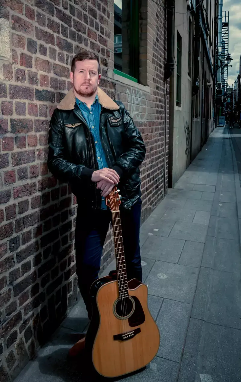 George Murphy with his guitar against a brick wall